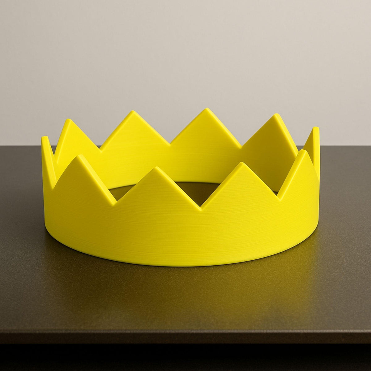 Yellow crown-shaped object on a dark surface with a neutral background