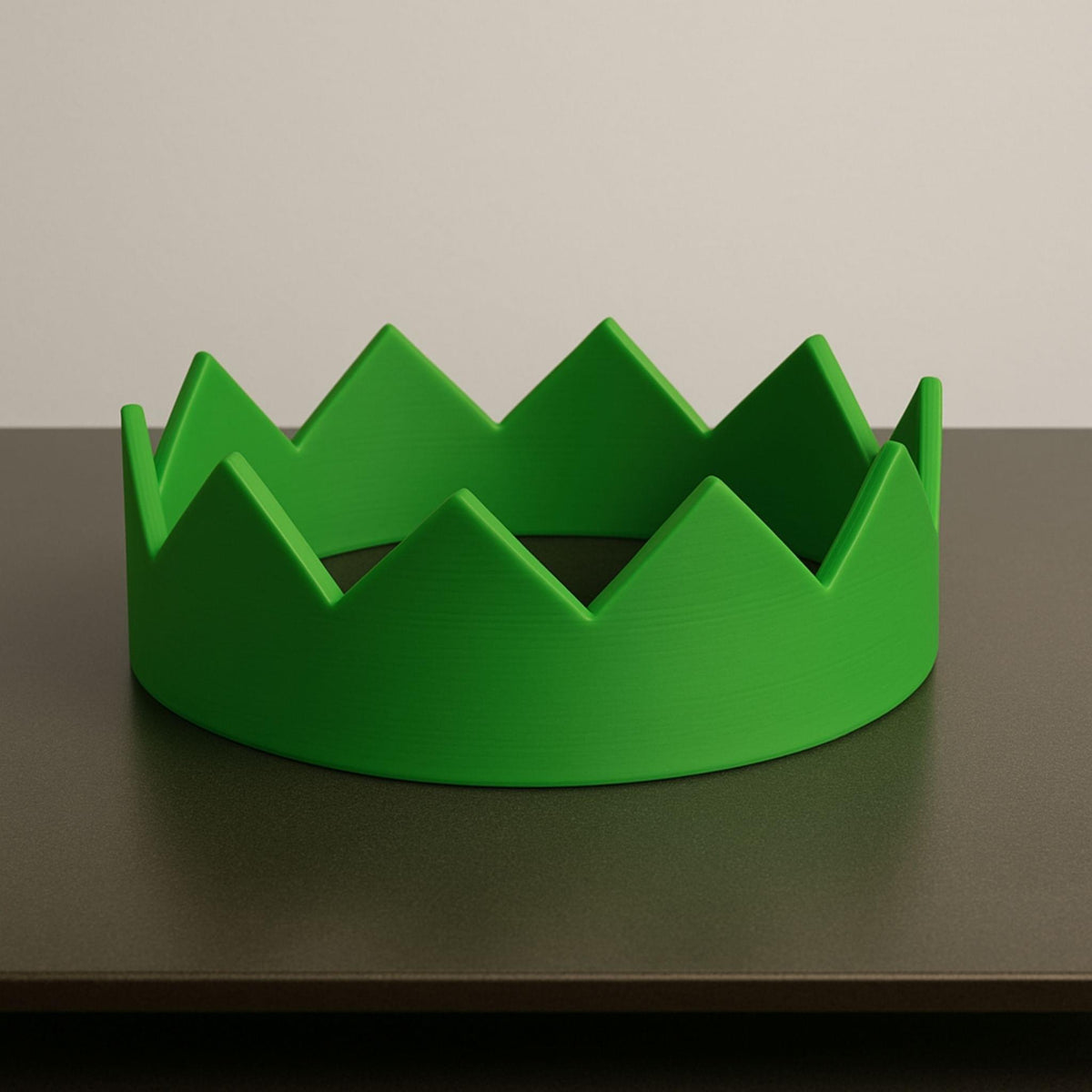 Green crown-shaped object on a dark surface with a neutral background